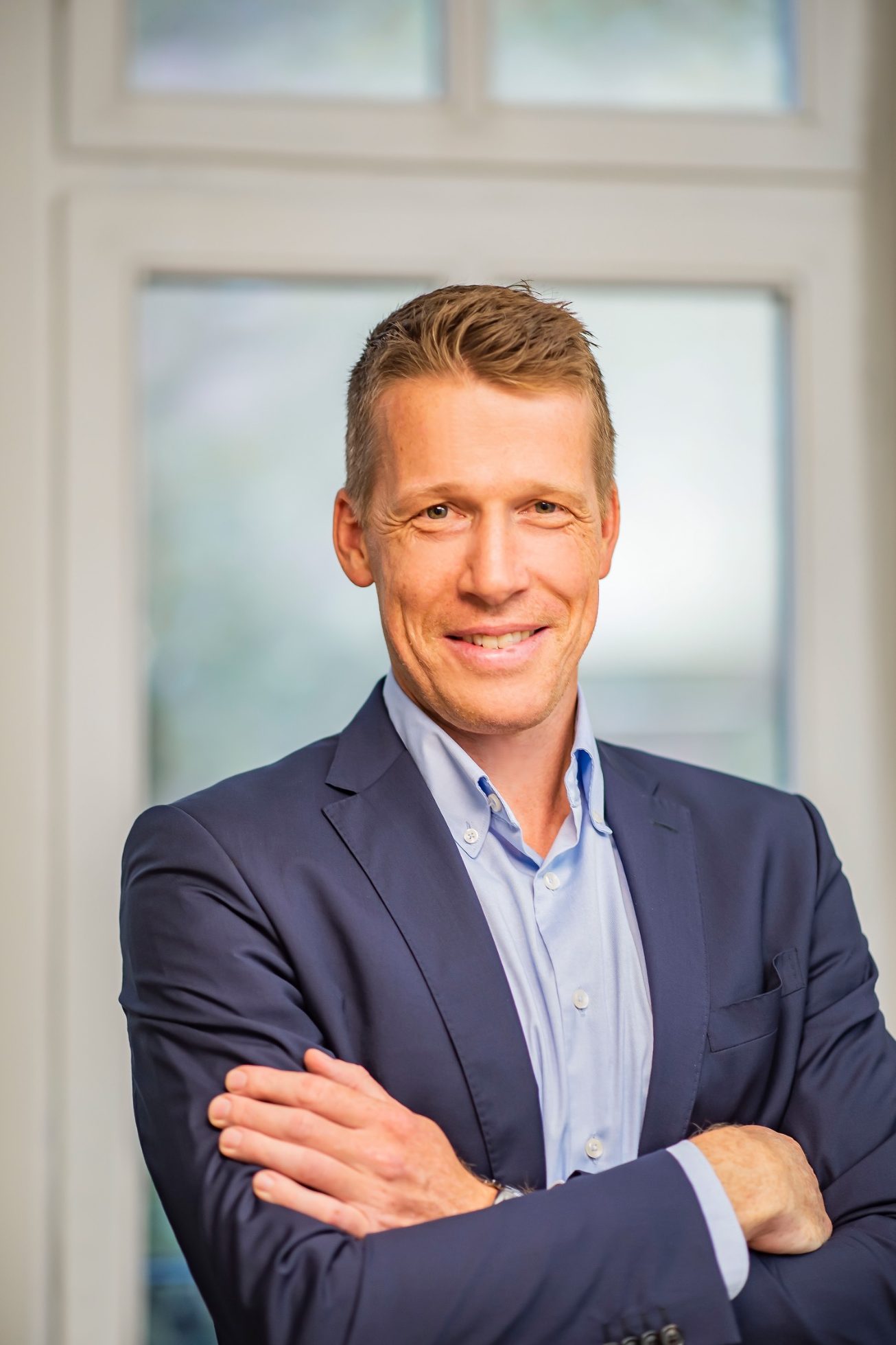 Götz, Lenas Männlicher Geschäftsmann in Anzug lächelt vor einem hellen Fenster.